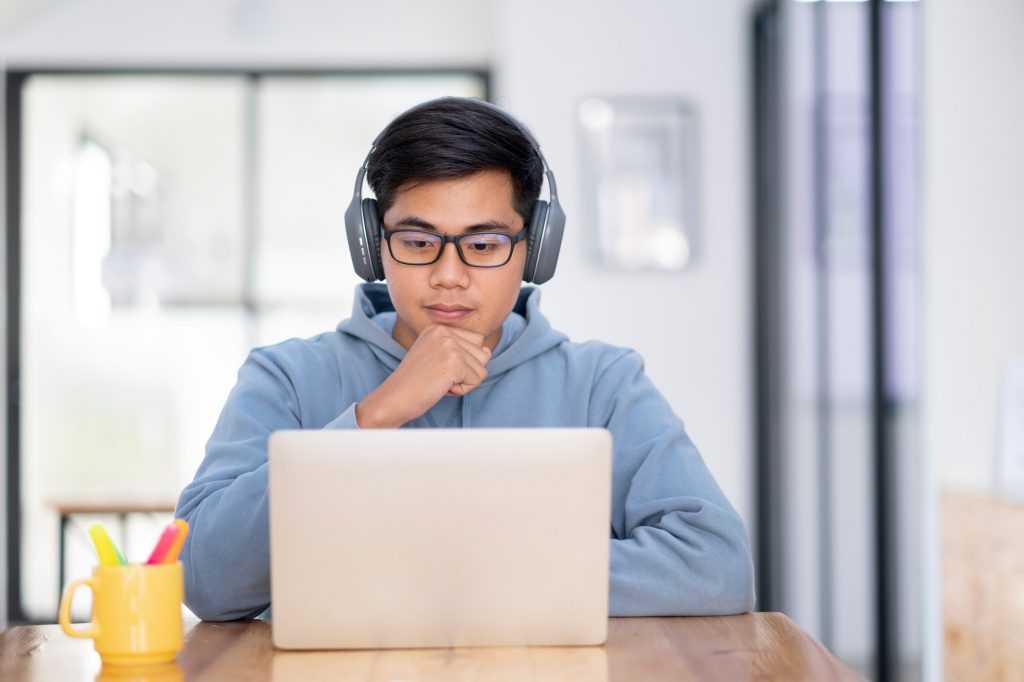 young asian student man wearing headset and looking at laptop display for learning online course